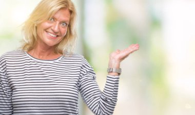 Orta yaş sarışın kadın neşeli sunulması ve kameraya bakarak avucunun ile işaret gülümseyen izole arka plan üzerinde.