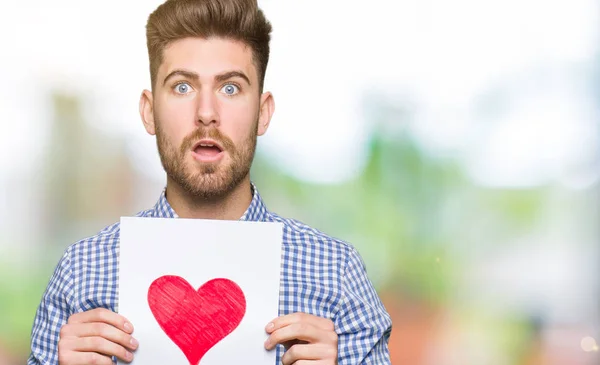 Jovem Homem Bonito Segurando Papel Com Coração Vermelho Assustado Choque — Fotografia de Stock