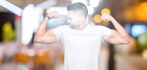 Jovem Vestindo Camiseta Branca Casual Sobre Fundo Isolado Mostrando Músculos — Fotografia de Stock