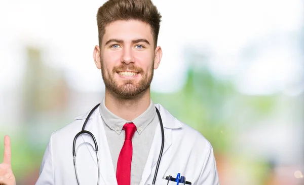 年轻英俊的医生男子穿着医疗外套显示和手指第二 而微笑着自信和快乐 — 图库照片