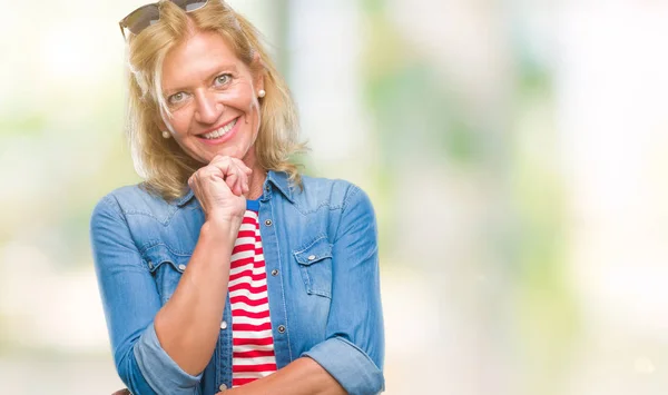Middle age blonde woman over isolated background looking confident at the camera with smile with crossed arms and hand raised on chin. Thinking positive.