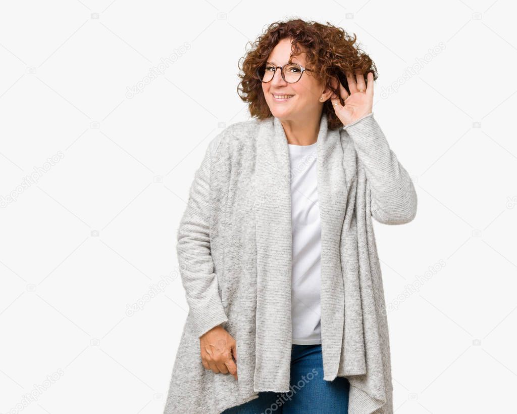 Beautiful middle ager senior woman wearing jacket and glasses over isolated background smiling with hand over ear listening an hearing to rumor or gossip. Deafness concept.