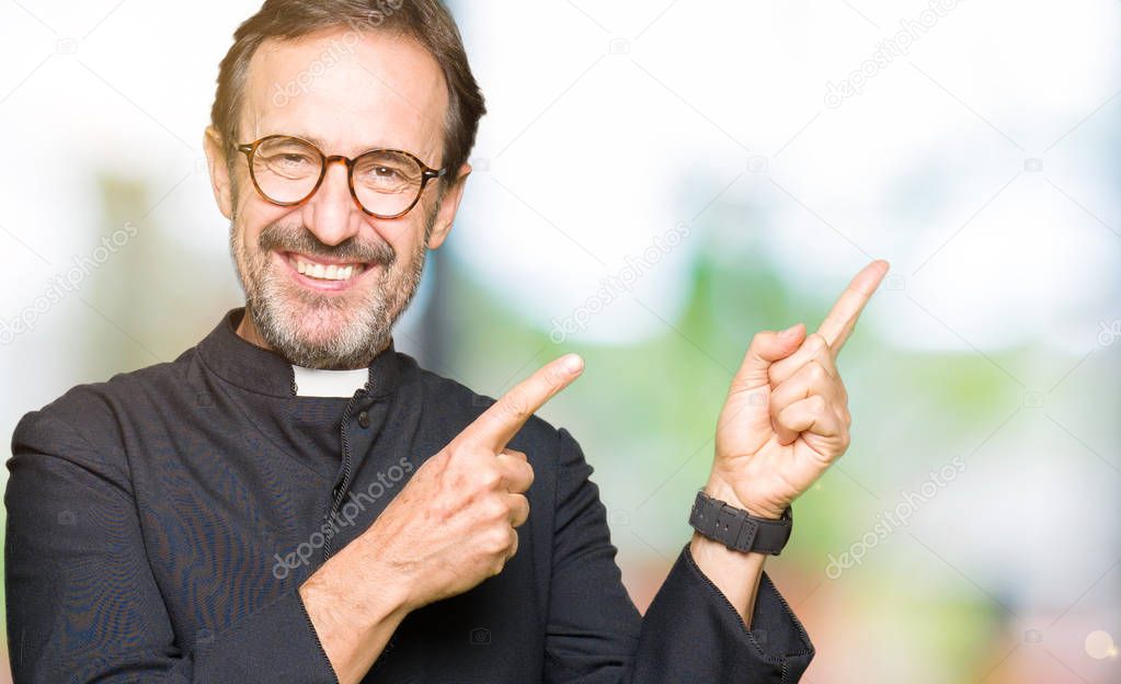 Middle age priest man wearing catholic robe smiling and looking at the camera pointing with two hands and fingers to the side.