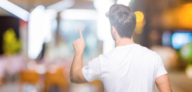 Beyaz t-shirt üzerinde izole giyen genç yakışıklı adam arka plan geriye doğru arkasında parmak eliyle işaret Posing