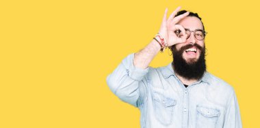 Uzun saç ve sakal gülümseyen, parmakları ile mutlu yüz üzerinden seyir göz el ile ok jest yapıyor gözlüklü genç hipster adamla.