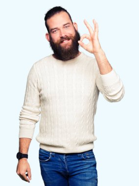 Genç hipster adam giyen kış kazak el ve parmaklar ok işaretiyle yapıyor olumlu gülümseyerek. Başarılı ifade.