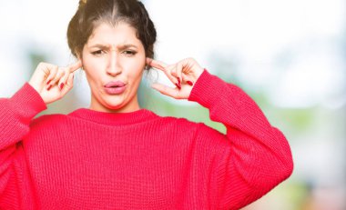 Kırmızı kazak ve yüksek sesle müzik gürültü rahatsız ifade parmaklarıyla kulaklarıyla kapsayan topuz giyen genç güzel kadın. Sağır kavramı.