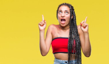 Genç örgülü saç Afrika kökenli Amerikalı pigmentasyon ile leke Doğum işareti hayrete ve yukarıya bakıyor ve parmakları ile işaret ve silah kaldırdı sürpriz izole arka plan üzerinde.