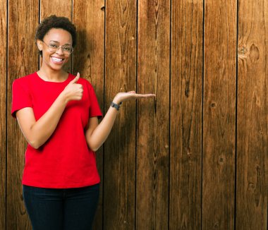 Güzel genç Afro-Amerikan kadın izole arka plan gösteren palm el ve iş tamam jestle üzerinde başparmak yukarı, gülümseyen mutlu ve neşeli gözlüklü