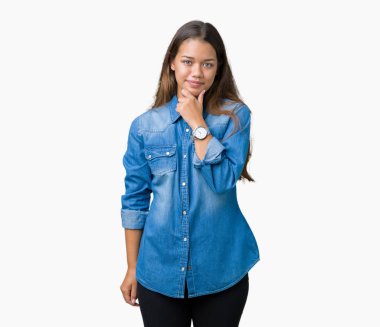 Genç güzel esmer kadın üzerinde mavi kot gömlek giymiş emin çapraz kollar ve çeneme kaldırdı el ile gülümseme ile kameraya bakarak arka plan izole. Pozitif düşünce.