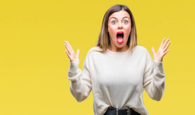 Genç güzel kadın rahat beyaz kazak üzerinde arka plan çılgın kutlama izole ve başarı için kaldırdı kollarını açarak hayrete ve heyecanlı çığlık gözleri açık. Kazanan kavramı