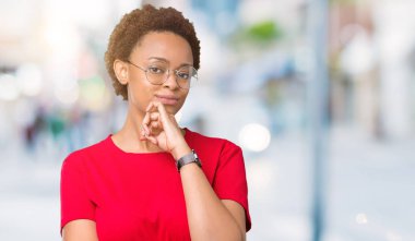 Emin çapraz kollar ve çeneme kaldırdı el ile gülümseme ile kameraya bakarak izole arka plan üzerinde gözlük güzel genç Afro-Amerikan kadın. Pozitif düşünce.