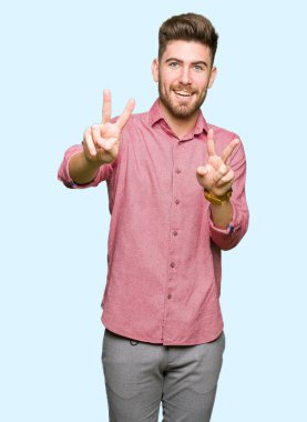 Genç yakışıklı iş casual adam zafer işareti yapıyor parmak gösterilen kamera seyir gülümseyerek. İki numaralı.