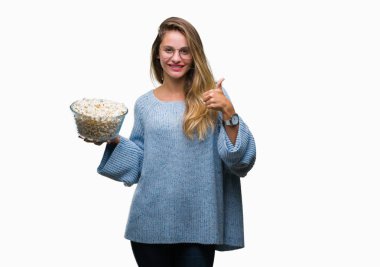 Genç güzel sarışın kadın ok işareti, başparmak ile parmak, mükemmel işareti yapıyor kocaman bir gülümseme ile izole arka plan üzerinde mutlu patlamış mısır yemek