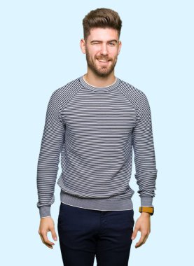 Çizgili süveter seksi bir ifadeyle, neşeli ve mutlu yüzünü kameraya bakarak göz kırpıyor giyen genç yakışıklı adam.