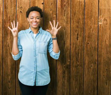 Gösterilen ve parmakları ile işaret izole arka plan üzerinde genç güzel bir Afrikalı-Amerikalı kadın numara 9 kendinden emin ve mutlu gülümseyerek süre.