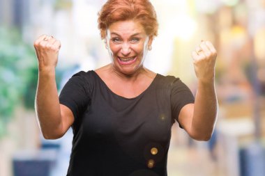 Gülümseyen ve başarı için çığlık Atrractive üst düzey beyaz Kızıl saçlı kadın izole arka plan çok mutlu ve heyecanlı kaldırdı, silah ile kazanan jest yapıyor. Kutlama kavramı.