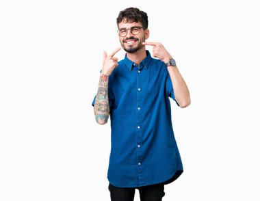Kendinden emin gösterilen ve işaret parmakları diş ve ağız ile gülümseyen izole arka plan üzerinde gözlük takan yakışıklı delikanlı. Sağlık kavramı.