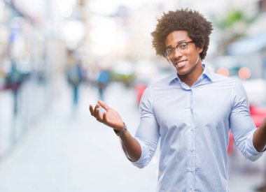 Afro Amerikan iş adamı izole arka plan clueless ve şaşkın bir ifadeyle kollar ve eller kaldırdı üzerinde gözlük takıyorum. Şüphe kavramı.