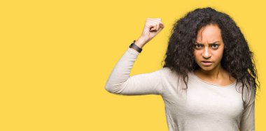 Öfkeli ve sinirli sinirli ve öfke ile bağırarak süre öfkeli yumruk yükselterek rahat kazak giyen kıvırcık saçlı Genç güzel kız. Öfke ve agresif kavramı.