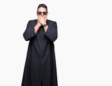 Genç Hıristiyan rahip giyen güneş gözlüğü izole arka plan ağız hata için elleriyle kapsayan şok içinde. Gizli kavramı.