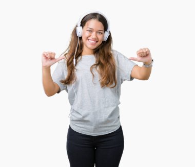 Yüzünde gülümseme ile kendinden emin görünüyorsun, kendini gururlu ve mutlu parmakları ile işaret izole arka plan üzerinde müzik kulaklık giyen genç güzel kadın.