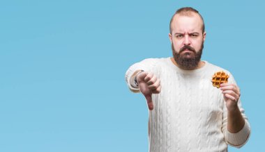 Genç beyaz hipster man kızgın yüzü, eksi işareti aşağı antipati başparmak ile gösterilen, ret kavramı ile izole arka plan üzerinde tatlı waffle yemek