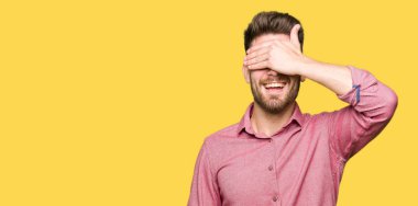 Genç yakışıklı iş casual adam gülümsüyor ve gözleri için sürpriz kapsayan yüz el ile gülüyor. Kör kavramı.