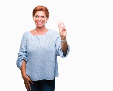 Gösterilen arka plan üzerinde kış kazak giyen Atrractive üst düzey beyaz Kızıl saçlı kadın izole ve parmakları ile işaret kendinden emin ve mutlu gülümseyerek iken üçüncü.