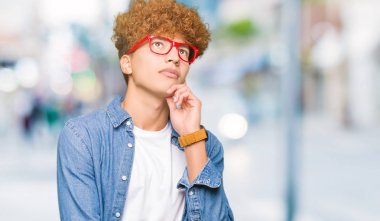 Yakışıklı genç afro saçlı gözlüklü el ile çene düşünme hakkında soru, dalgın ifade üzerine. Düşünceli yüzüyle gülümsüyor. Şüphe kavramı.