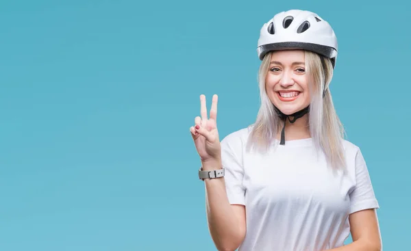 年轻的金发女子穿着自行车安全头盔在孤立的背景微笑着快乐的脸眨眼在相机做胜利标志 第二个 — 图库照片