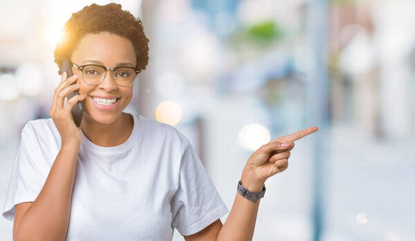 Молодая африканская американка, разговаривающая по телефону на изолированном фоне, очень довольна, указывая рукой и пальцем в сторону.
