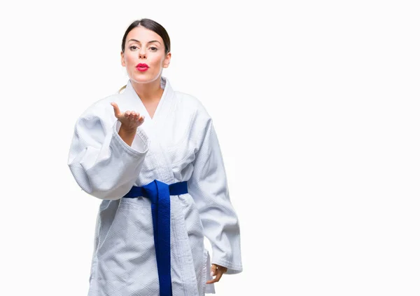 Young beautiful woman wearing karate kimono uniform over isolated background looking at the camera blowing a kiss with hand on air being lovely and sexy. Love expression.