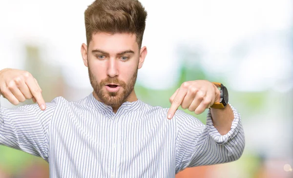 Young handsome man Pointing down with fingers showing advertisement, surprised face and open mouth