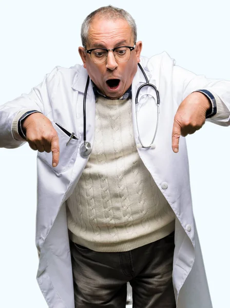 穿着医疗外套的英俊的资深医生用手指指着广告 惊讶的脸和张开的嘴 — 图库照片