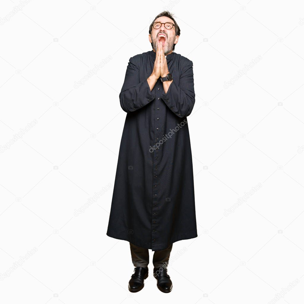 Middle age priest man wearing catholic robe begging and praying with hands together with hope expression on face very emotional and worried. Asking for forgiveness. Religion concept.