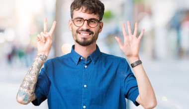 Gösterilen arka plan üzerinde gözlük takan genç yakışıklı adam izole ve parmakları ile işaret kendinden emin ve mutlu gülümseyerek süre yedi numara.