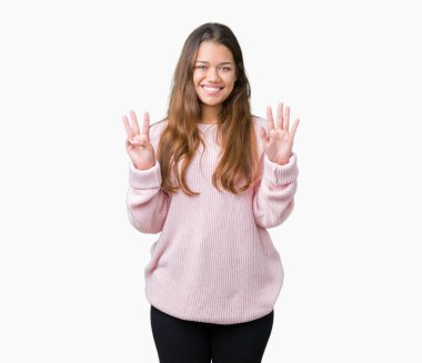Gösterilen ve parmakları ile işaret izole arka plan üzerinde pembe kış kazak giyen genç güzel esmer kadın kendinden emin ve mutlu gülümseyerek süre sekiz numara.