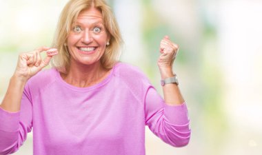 Duygu tezahürat gurur çığlık ve zafer ve başarı çok heyecanlı, kutluyor izole arka plan üzerinde pembe macaron bisküvi yediğine orta yaş sarışın kadın