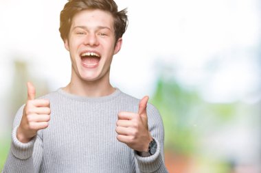 El ile pozitif jest yapıyor izole arka plan başarı işareti üzerinde kış kazak giyen genç yakışıklı adam başparmak gülümseyen ve mutlu. Neşeli bir ifadeyle, kazanan jest kameraya bakıyor.