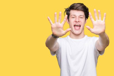 Gösterilen ve parmakları ile işaret izole arka plan üzerinde rahat beyaz t-shirt giyen genç yakışıklı adam kendinden emin ve mutlu gülümseyerek süre on numara.