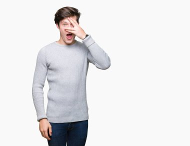 Mahcup ifadeyle parmaklarımın arasından seyir yüz ve gözler el ile kapsayan şok bakmak izole arka plan üzerinde kış kazak giyen genç yakışıklı adam.