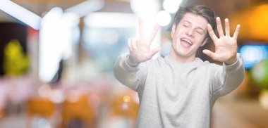 Gösterilen arka plan üzerinde sweatshirt giyen genç yakışıklı sportif adam izole ve parmakları ile işaret kendinden emin ve mutlu gülümseyerek süre 8 numaralı.