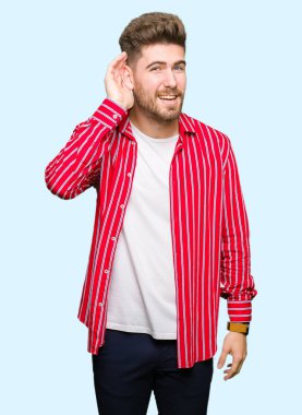 Genç yakışıklı bir işitme söylenti ya da dedikodu için dinleme kulak üzerinde el ile gülümseyen giyen kırmızı gömlekli adam. Sağırlık kavramı.