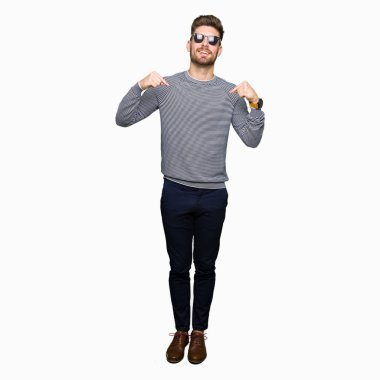 Yüzünde gülümseme ile kendinden emin görünüyorsun, kendini gururlu ve mutlu parmakları ile işaret giyen güneş gözlüğü genç yakışıklı adam.