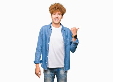 Seyir ve başparmak yanında yukarıyı mutlu yüz ile gülümseyen denim ceket giyen afro saçlı Genç yakışıklı adam.
