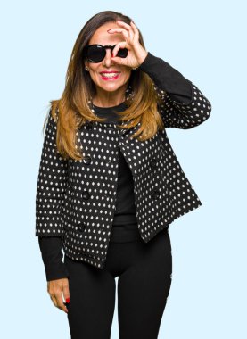 Güzel orta yaş kadın giyiyor güneş gözlüğü el gülümseyen, ok jest yapıyor göz parmakları ile mutlu yüz üzerinden seyir.