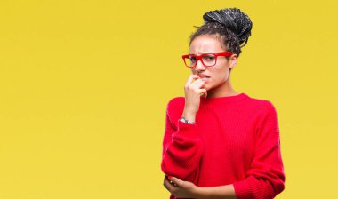 Kazak ve gözlük stresli ve gergin elle çivi ısırma ağzına bakarak izole arka plan üzerinde giyen genç örgülü saç Afrikalı-Amerikalı kız. Anksiyete sorunu.