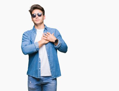 Yakışıklı delikanlı ile gülümseyen izole arka plan üzerinde güneş gözlüğü takıyor kapalı gözler ve yüzünde minnettar jest ile göğüs üzerinde eller. Sağlık kavramı.