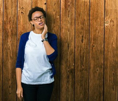 Diş ağrısı veya dişlerde dişlerle ilgili hastalık nedeniyle ağız acı ifadesi ile el ile dokunmak izole arka plan üzerinde gözlük takan genç güzel Afrikalı-Amerikalı kadın. Diş hekimi kavramı.